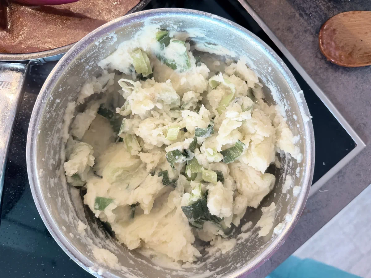 Lauch-Kartoffelstampf mit hellgrünen Lauchringen im Edelstahltopf, oben links eine Pfanne mit der Soße
