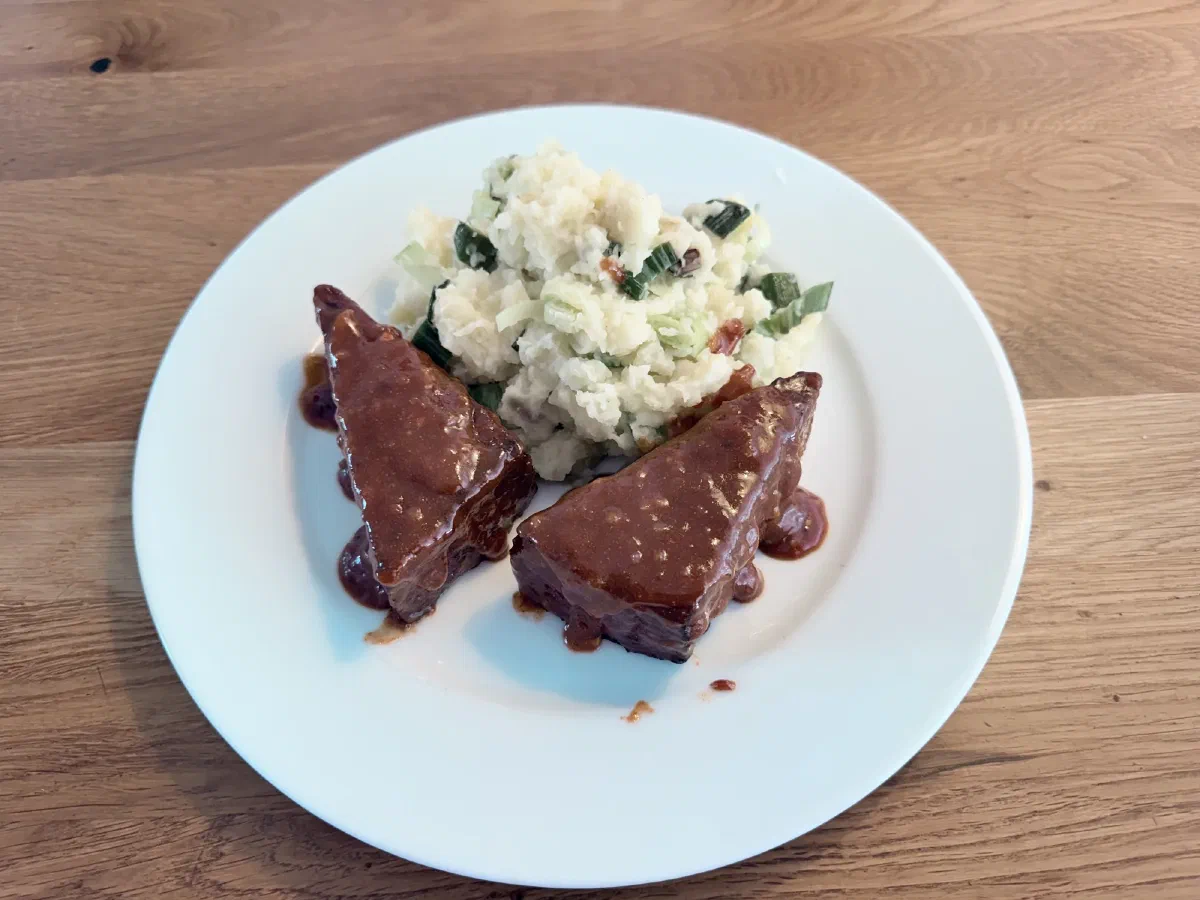 Zwei Tofu-Dreiecke mit dunkelroter, glänzender Glaze neben Lauch-Kartoffelstampf auf einem weißen Teller auf einem Holztisch