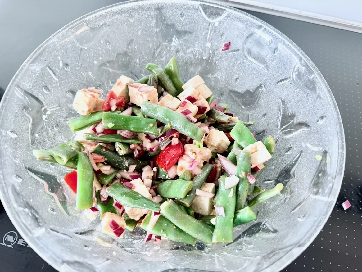 Warmer Bohnensalat in einer Glasschüssel: grüne Bohnen mit roten Zwiebelwürfeln, halbierten Kirschtomaten und hellen Fetawürfeln